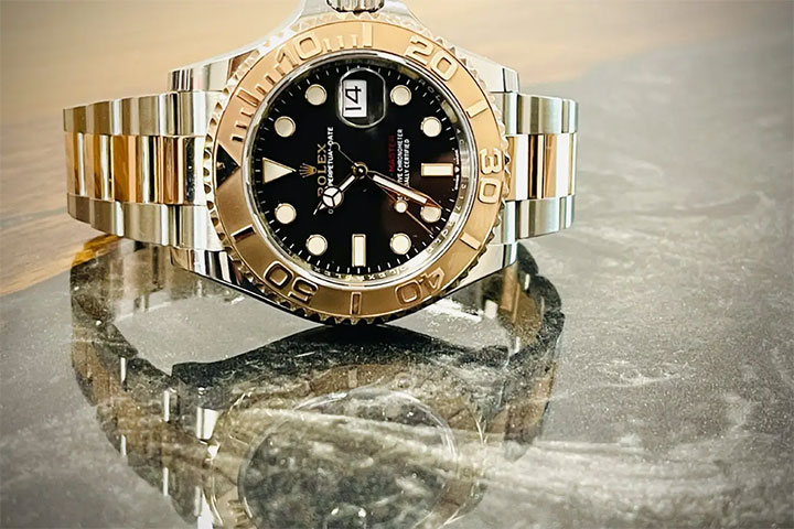 A two-tone wristwatch with a black dial and date display on a reflective surface